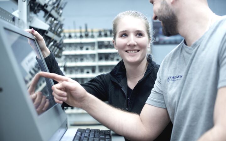 Zwei Mitarbeiter aus der Produktion unterhalten sich gut gelaunt vor einem PC-Terminal